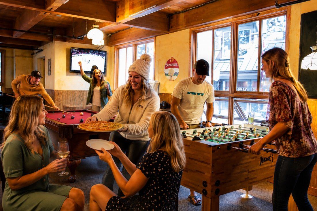 Friends playing pool and foosball with pizza and drinks